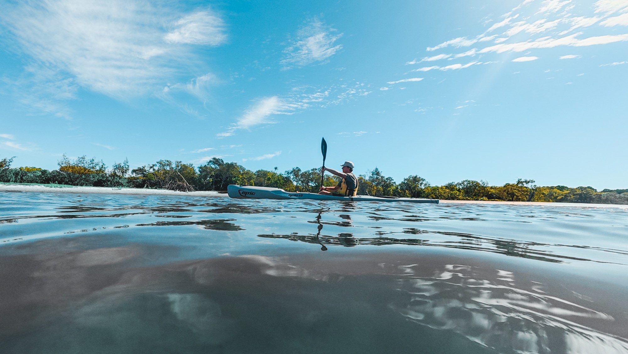 Person kayaking on calm water under a blue sky with light clouds.